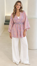 Front view of model wearing pink paisley print belted kimono cardigan with white wide-leg trousers