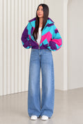 Front full view of woman wearing purple and turquoise retro colorblock windbreaker jacket with wide-leg jeans