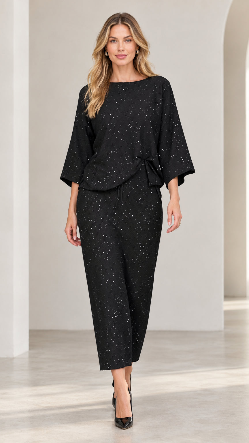 Front view of model wearing black shimmer speckled two-piece top and pant set with black heels