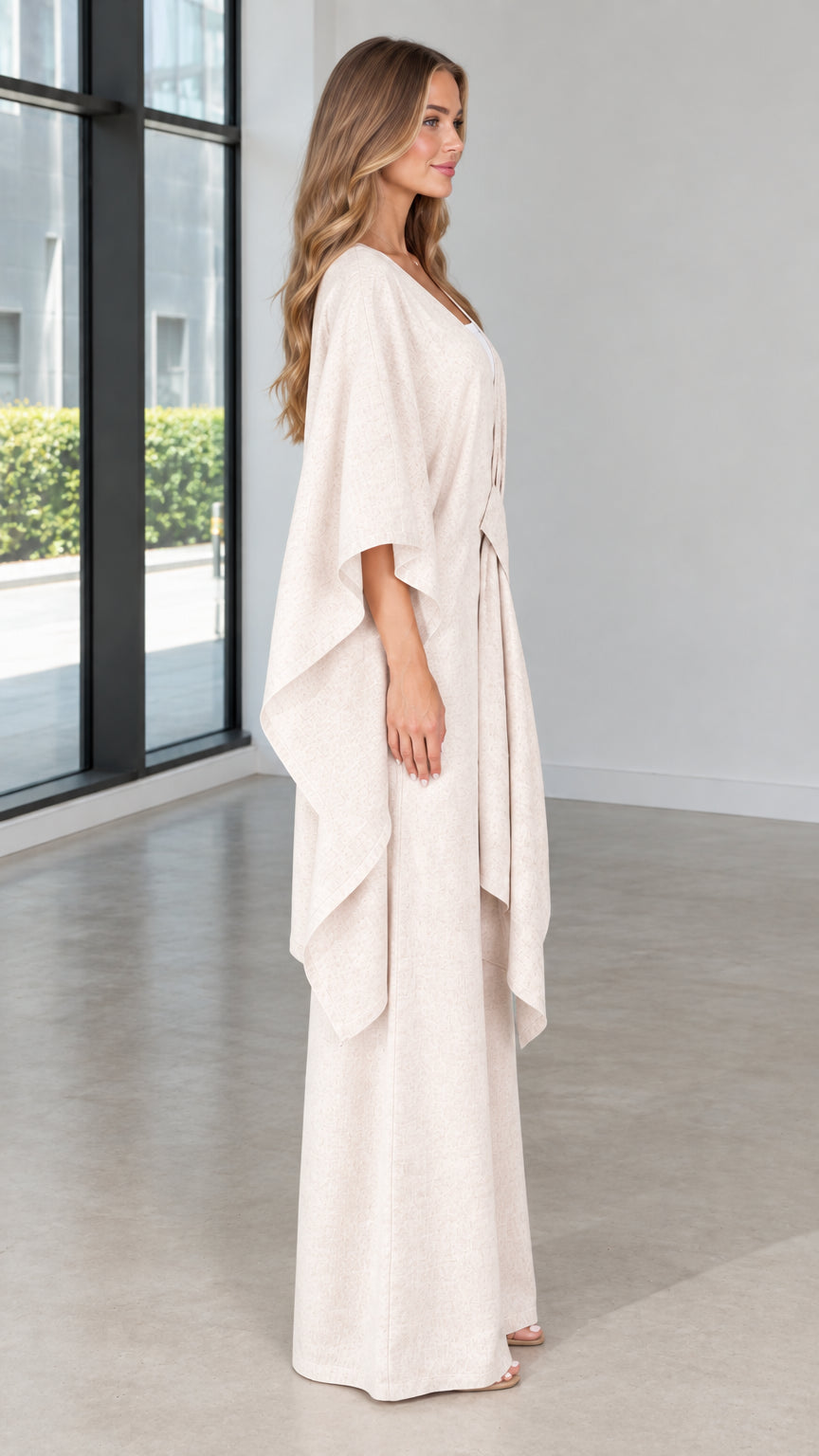 Side view of woman wearing beige relaxed cape top and matching trousers
