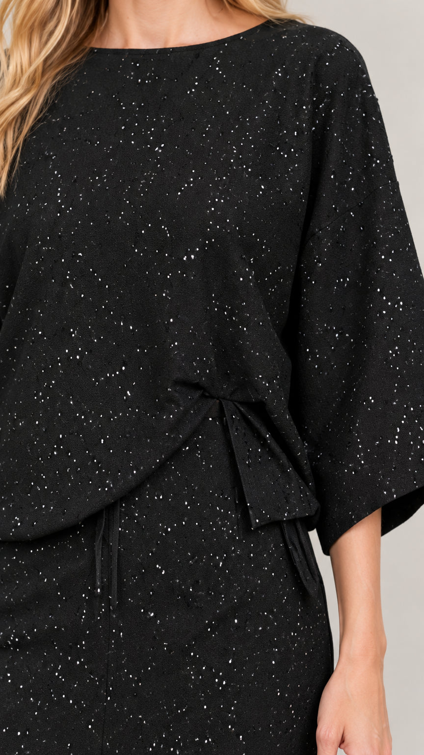 Close-up detail of side-knot waist accent and speckled fabric texture on black top