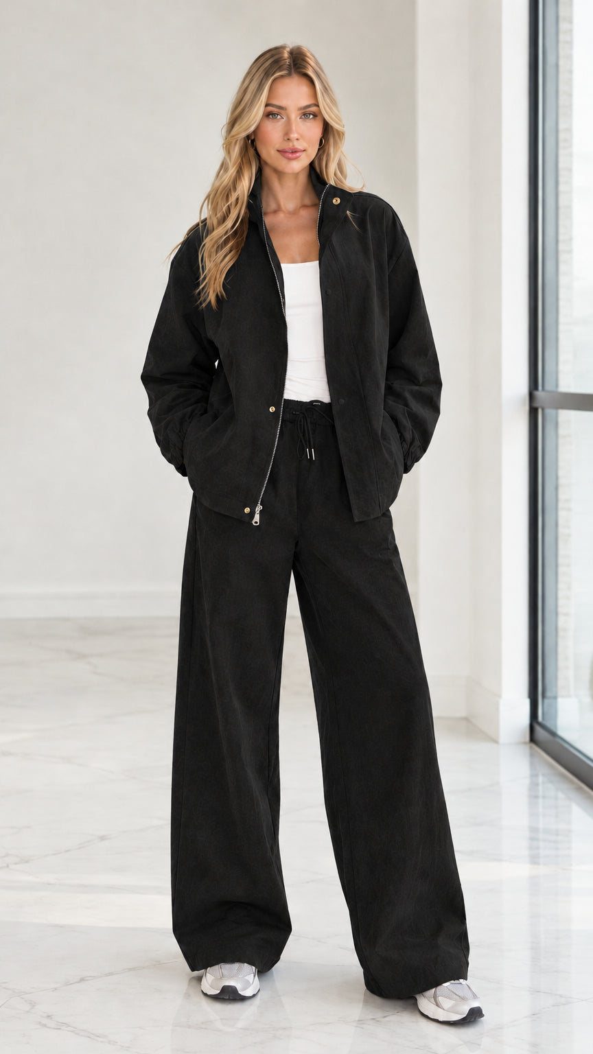 Full front view of woman wearing black 2-piece zip jacket and wide leg pants set